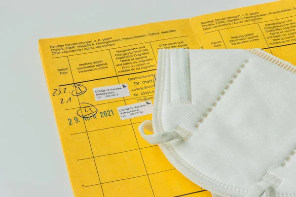 Yellow international vaccination certificate with vaccinations against coronavirus. Double AstraZeneca vaccination on sheet from WHO passport. White FFP2 mask on the vaccination card