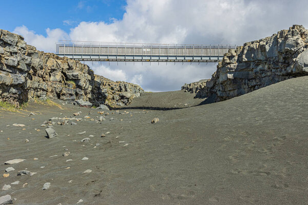 black lava sand with bridge on Iceland of Reykjanes Peninsula. Geographical fissures of the North American and Eurasian plates. Lava stone walls in sunshine