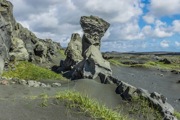 Landscape on Iceland. Lava rocks and lava sand from Reykjanes Peninsula in the day in sunshine with clouds. Rock needle and volcanic rock wall with green grass