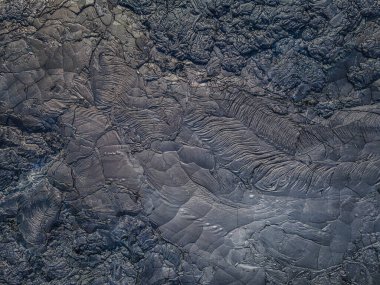 Katı lavın üst görüntüsü. Lav akışından gelen koyu renkli yapılar. Ertelenmiş ve kırılmış taşlar. Grinin farklı tonları. Dalgalı ve pürüzlü sert lav alanı