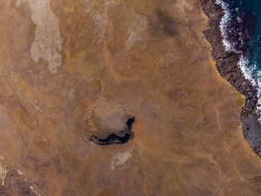 İzlanda 'da aktif olmayan volkanik krater. Reykjanes Yarımadası 'nın en iyi manzarası. Bir sahil şeridinde kum yüzeyi. Kraterde güneş ışığı ve gölgeler belirdi. Sakin bir denizde dalgalar ve uçurumlar