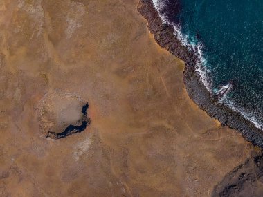 Yukarıdan etkin olmayan volkanik krater. İzlanda 'nın Reykjanes Yarımadası' nın insansız hava aracı manzarası. Güneş doğduğunda kraterin etrafında gölgeli kahverengi kum yüzeyi. Dalgalı ve kayalıklı kıyı şeridi