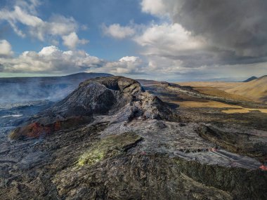 İzlanda 'nın Reykjanes Yarımadası' ndaki aktif kraterlerle manzara. Kraterin etrafında tek tek buhar kolonları olan soğutulmuş lav akışı. Bulutlar ve mavi gökyüzü ile gün ışığı.