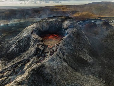 İzlanda 'da ağzında kırmızı lavla kratere bak. Gündüzleri Reykjanes Yarımadası 'nda volkanik krater. Patlamadan önce krater. Kraterin etrafında koyu soğumuş lav ve arkasında sarı kahverengi tepeler var.