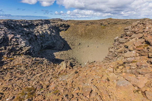 View of a crater of a volcano on Iceland\'s Reykjanes peninsula. Landscape with brown and gray lava rocks and along the rim of the crater. Nature at day with sunshine and clouds in the sky