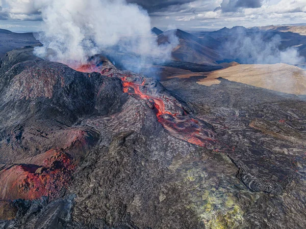 liquid magma flows from the volcanic crater. Volcano on Iceland\'s Reykjanes Peninsula. green, red gray and dark lava rocks around the crater. Steam and clouds in the sky in daylight