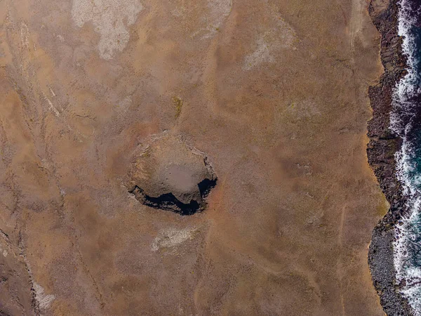 Top view on landscape of Iceland. Old crater on brown sand surface on coast of Reykjanes Peninsula. Waves and Water with Shoreline. Craters with shadows in sunshine