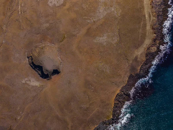 landscape in Iceland. Top view of extinct crater. Volcanic crater with shadows in sunshine. brown sand surface on coast of Reykjanes Peninsula. Waves and water at the shoreline with cliffs.
