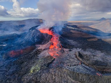Lava flow with glowing hot magma at volcanic eruption in Iceland. View into the volcanic crater from above during the day. Landscape on the Reykjanes Peninsula. Smoke and steam near the crater
