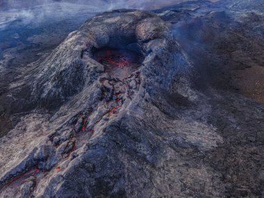 Volkanik kraterin görüntüsü. Kraterin ağzında kırmızı lav yapıları. Volkan patlamadan hemen önce. Kraterin etrafındaki karanlık, soğutulmuş magma kayaları. Buhar ve duman kraterlerin yanında.