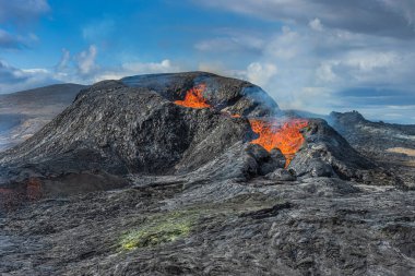 İzlanda 'nın Reykjanes Yarımadası' nda aktif volkan. Baharda güneşli manzara. Sıvı lav kraterin kenarından dışarı akar. Biraz buhar çıkıyor. Gökyüzündeki bulutlar.
