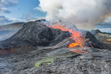 İzlanda 'daki bir volkandan lav akışı. Reykjanes Yarımadası 'ndaki volkanik manzara. Volkanın etrafındaki soğuk, gri, kırmızımsı, yeşil volkanik kayalar. Volkanik kraterin üzerinde buhar oluşumu.