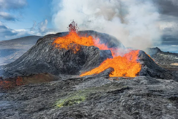 Active volcano on Iceland\'s Reykjanes Peninsula. Small lava fountain from the crater. Landscape in spring with sunshine. Liquid lava flows out of the side of the crater. Steam rises from crater