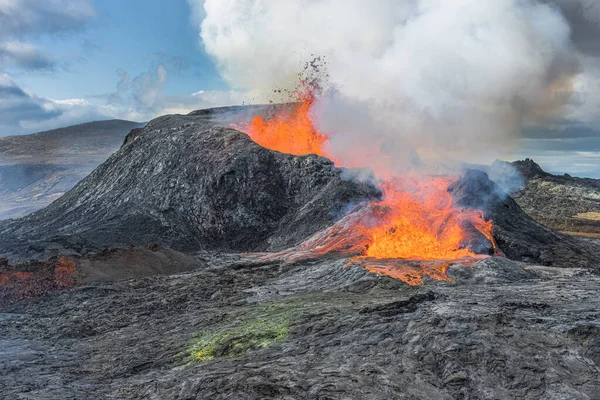 Volcano eruption in Iceland. active volcano with lava fountain. Lateral outflow of the hot reddish lava. View of volcano in the day with sunshine. clouds in the blue sky