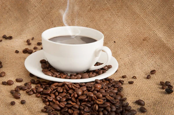Κύπελλο με κόκκους καφέ και καφέ και ατμού πάνω από το κύπελλο στο φόντο λινάτσα — Φωτογραφία Αρχείου