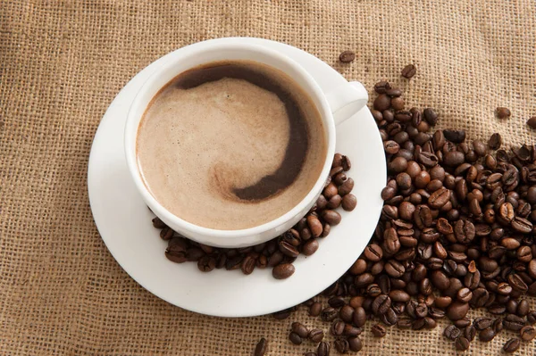 バーラップの背景にコーヒー豆とコーヒーのカップ — ストック写真