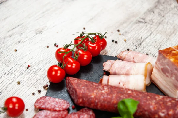 Smoked sausage, meat, bacon with basil and cherry tomatoes — Stock Photo, Image