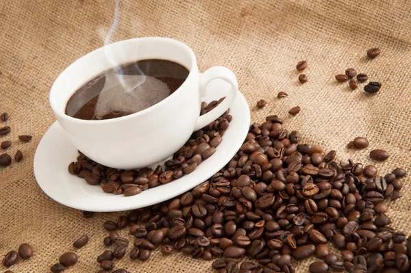 Ένα φλιτζάνι καφέ σε ένα πιατάκι με κόκκους καφέ σε φόντο λινάτσα — Φωτογραφία Αρχείου