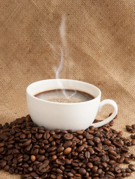 Taza de café en un platillo con granos de café sobre un fondo de arpillera — Foto de Stock