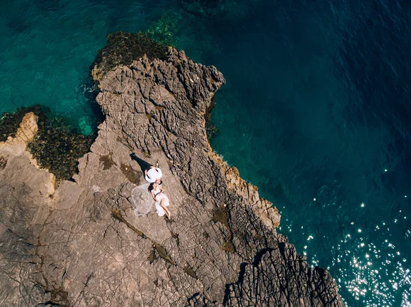 A noiva e o noivo deitam-se lado a lado na costa rochosa e olham um para o outro, vista superior — Fotografia de Stock