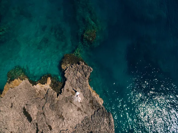 A noiva e o noivo deitam-se lado a lado na costa rochosa e olham um para o outro, vista superior — Fotografia de Stock