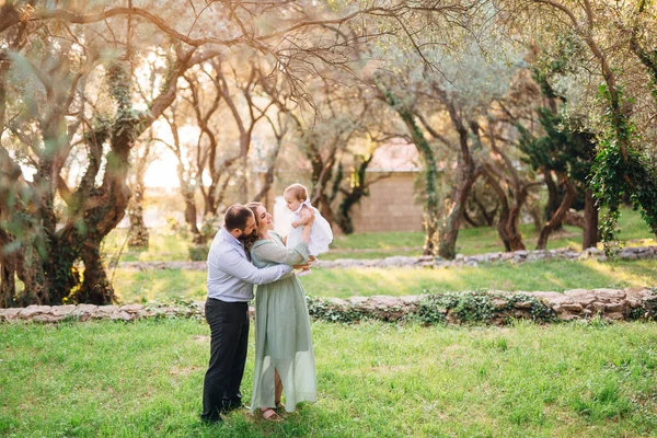 Budva, Montenegro - 01.06.17: Papai abraça mãe sorridente por trás, que está segurando uma garota em seus braços enquanto está de pé no parque — Fotografia de Stock