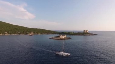 Beyaz yelkenli yat Zhanic adasının yanından geçiyor ve açık denize gidiyor.