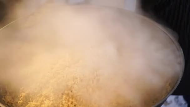 주방장은 우즈베키스탄의 필라 프를 큰 가마솥에 담긴 큰 숟가락 과섞는다 — 비디오