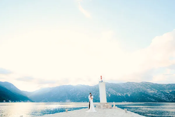 在灯塔的背景下，新婚夫妇拥抱在Gospa od Skrpjela岛上 — 图库照片