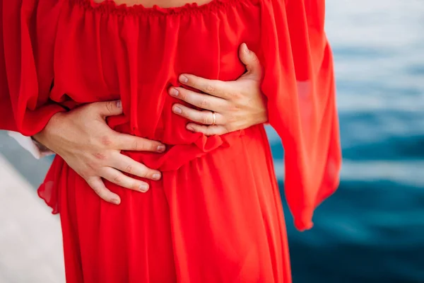 Las manos de los hombres abrazan a una mujer con un vestido rojo alrededor de la cintura. Primer plano — Foto de Stock