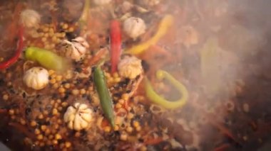 Özbek pilavı sarımsak başları, biber kabukları ve baharatlarla dolu bir kazanda pişiriliyor