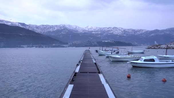 Pier met afgemeerde boten in Budva tegen de achtergrond van besneeuwde bergen — Stockvideo