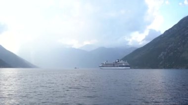 Büyük yolcu gemisi körfez boyunca dağların arka planına doğru yelken açıyor. Karadağ