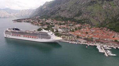 Eski Kotor kasabasının turuncu çatılarının insansız hava aracı görüntüsü ve kıyıya demirlemiş bir yolcu gemisi.