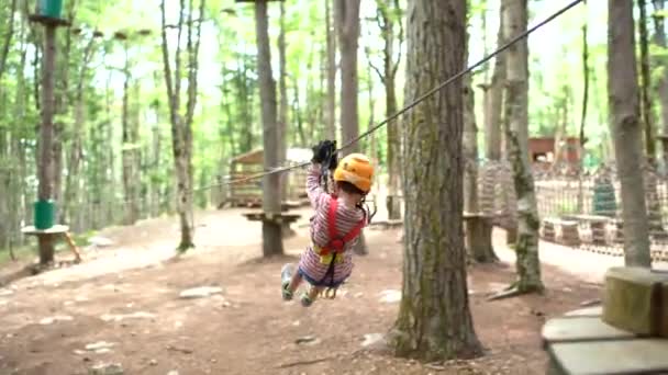 Мальчик с защитной веревкой едет по канату между деревьями. Вид сзади — стоковое видео