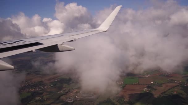 Vliegtuigvleugel in de lucht boven velden en gebouwen door de wolken — Stockvideo