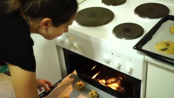 Meisje zet een bakplaat van Amerikaanse chocolade chip koekjes in een voorverwarmde oven — Stockvideo