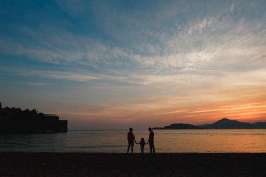 Annem ve babam gün batımında deniz kenarındaki çakıl taşı plajında el ele tutuşuyorlar.