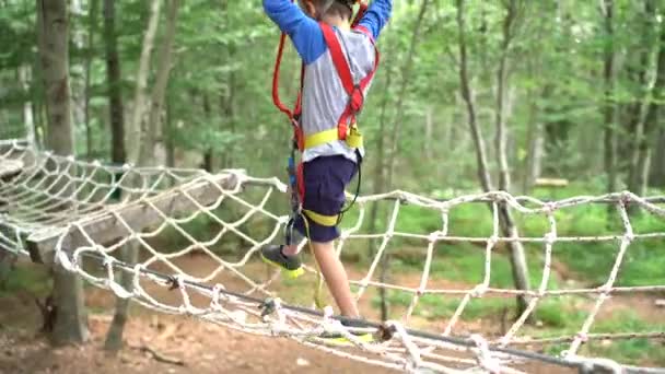 Мальчик движется по мосту сетки, держа верёвку — стоковое видео