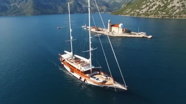 Biały jacht żaglowy przepływa wyspę Gospa od Skrpjela. Perast, Czarnogóra — Wideo stockowe