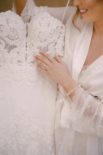 Bride in a robe holds a wedding dress on a hanger — Stock Photo, Image