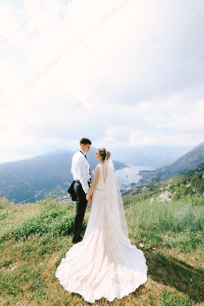 Wedding couple hold hands on the top of Mount Lovcen against the backdrop of the Kotor bay. Montenegro