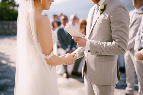 Groom lit un vœu de la carte à la mariée, tenant sa main — Photo