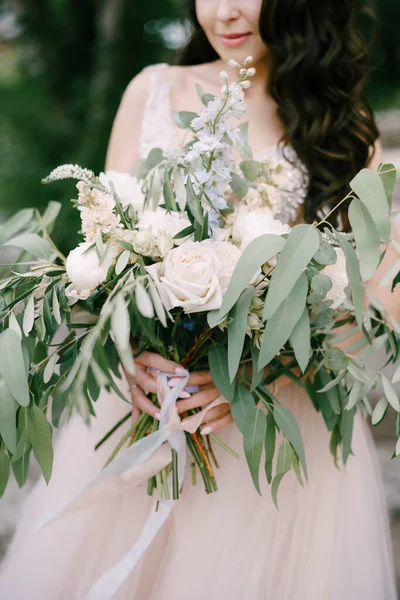 Pengantin wanita berdiri dengan karangan bunga mawar putih, poni, delphinium dan cabang eukaliptus di tangannya, close-up — Stok Foto