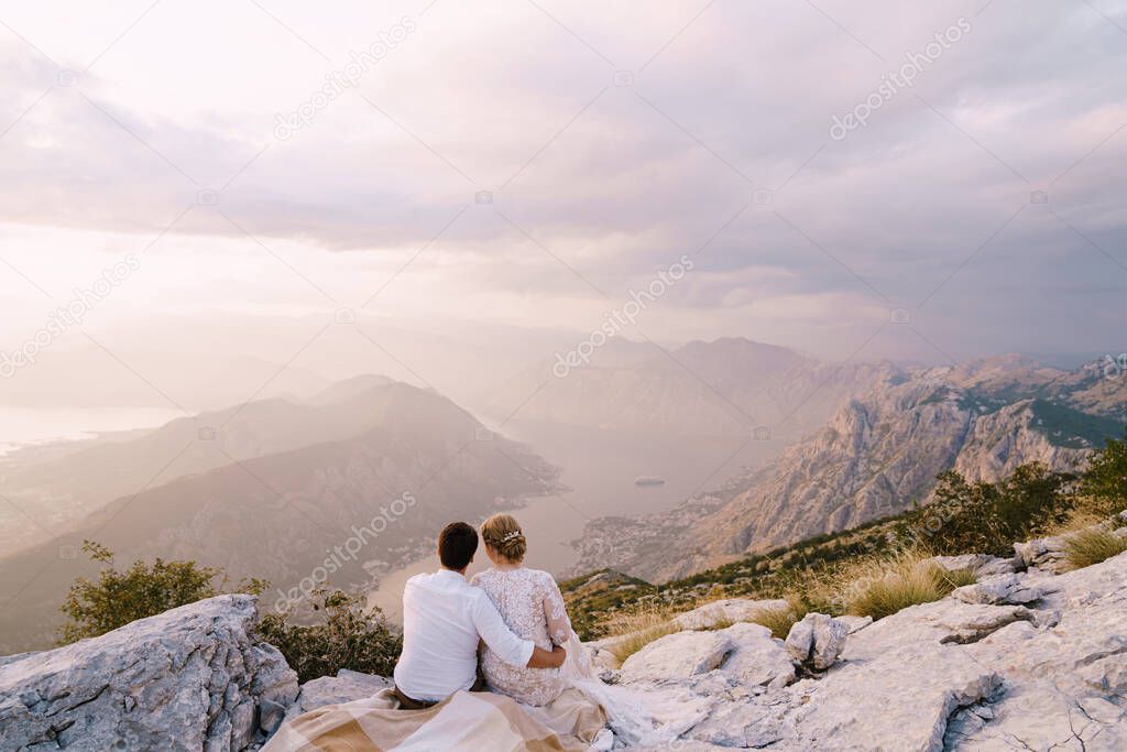 Bride and groom sit on the mountain and look at the bay