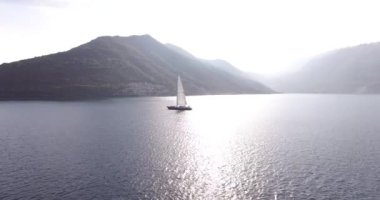 Beyaz yelkenli, sisli dağların arka planında denizde yüzüyor.