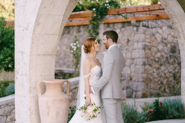 Noiva e noivo com um suporte de buquê sob um belo arco de pedra — Fotografia de Stock