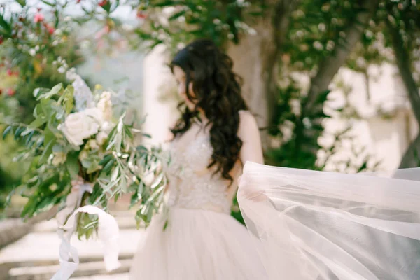 Pengantin wanita berdiri di bawah sebuah oleander mekar dengan buket pengantin, rok bergetar di belakangnya — Stok Foto