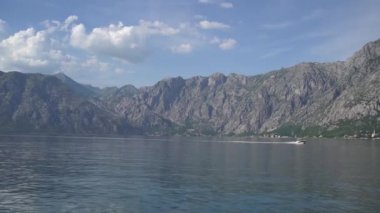 Motorlu tekne, Kotor Körfezi boyunca dağların arka planına doğru yelken açar.