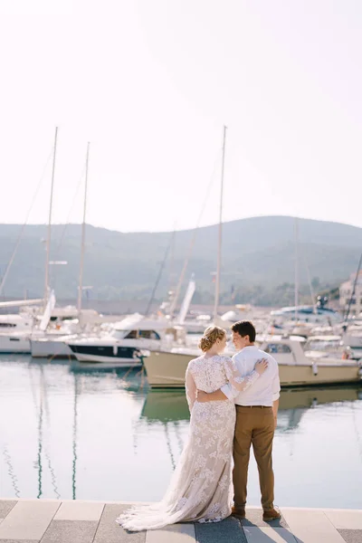 Noivo abraços noiva no cais junto ao mar em frente aos iates estacionados — Fotografia de Stock